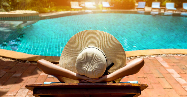woman in pool relaxing resting in vacation on summer season with hat at resort swimming pool edge with chair beach on side
